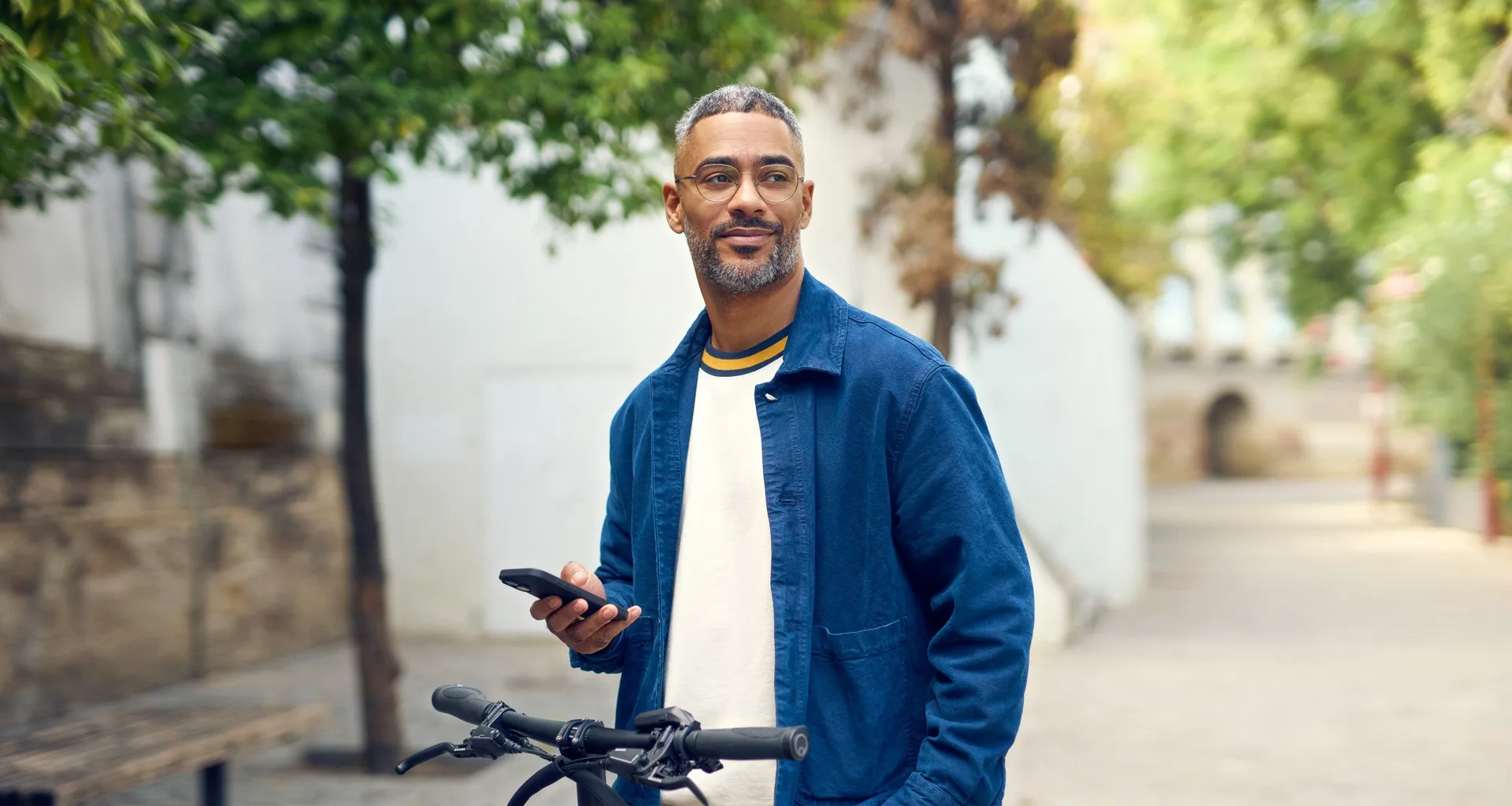 Salarié consultant son téléphone à côté de son vélo électrique Riese & Müller dans une rue arborée. Photo : Riese & Müller