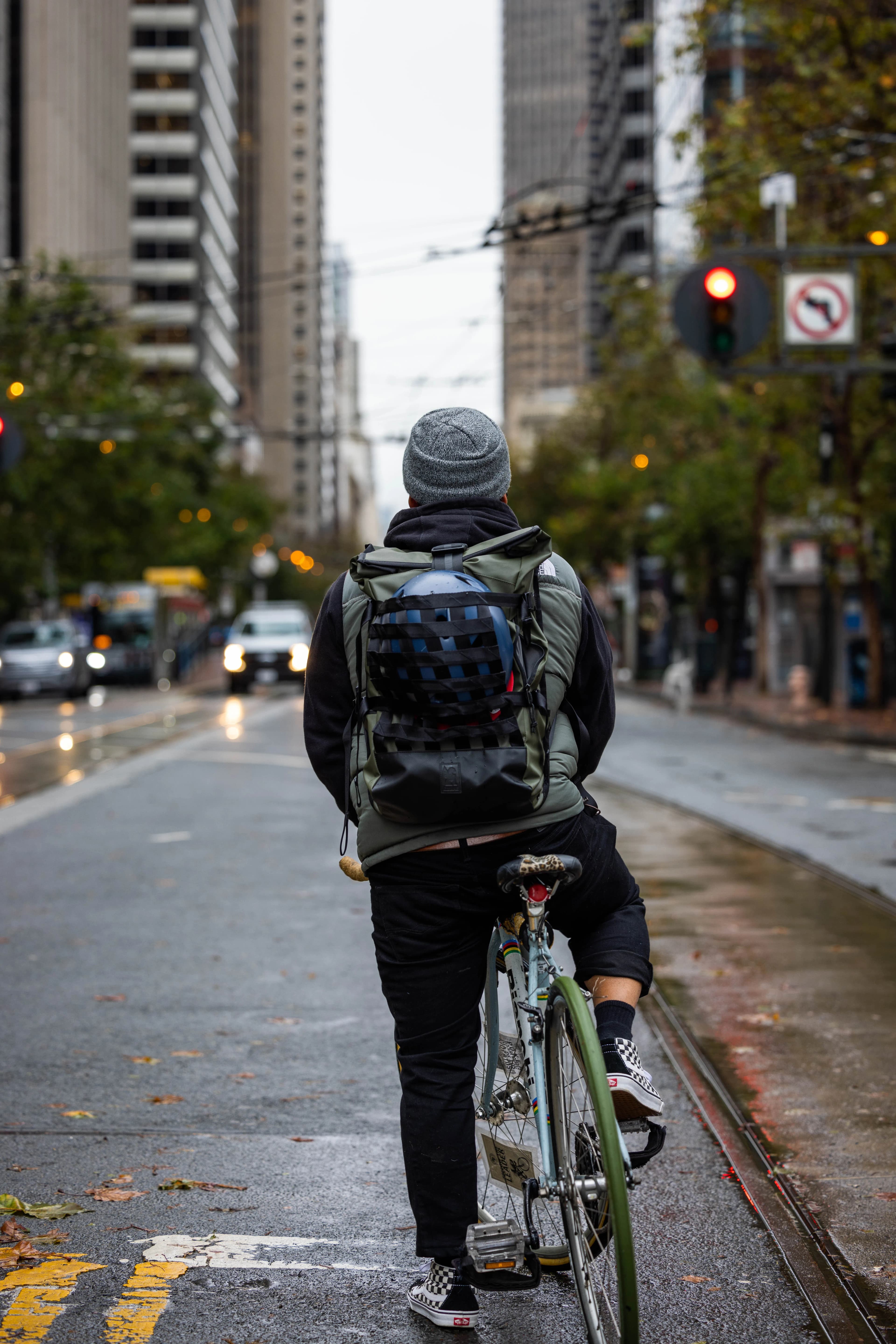 Cycliste vu de dos, sac sur le dos, sur une piste cyclable entre les immeubles.