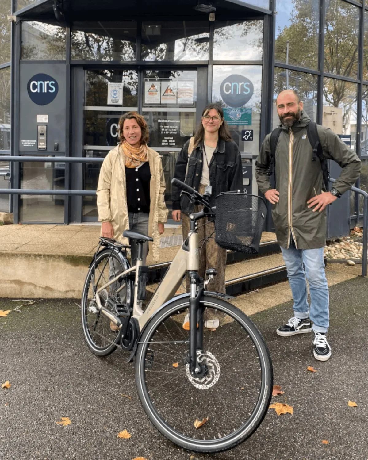 Trois personnes, dont une avec un vélo électrique, devant un bâtiment du CNRS.