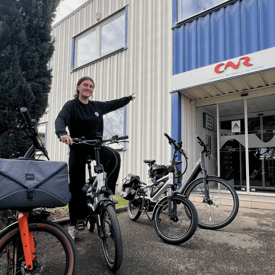A smiling woman on a bicycle points to the right in front of the CNR building.