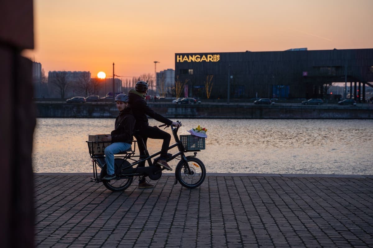 Cycliste et passager sur un vélo cargo Moustache Lundi 20 Cargo, sur un quai au coucher du soleil.